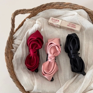 Three elegant French satin bow banana hair clips in red, pink and black on a rustic tray