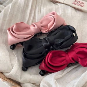 Three elegant satin bow banana clips in pink black and red on a soft fabric