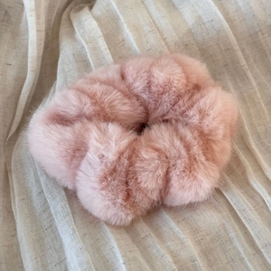 Detailed view of pink faux fur scrunchie with fluffy texture on soft beige fabric