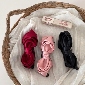 Close-up of three satin bow banana hair clips in burgundy pink and black colors