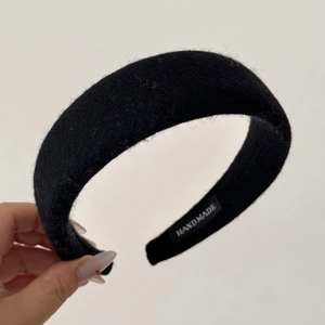 Detail view of a thick black handmade headband with textured wool fabric and handmade label