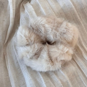 Detailed view of beige plush faux fur scrunchie on soft pleated fabric background