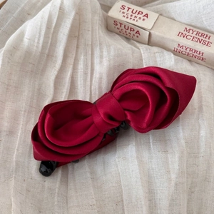 Close-up of a large red satin bow banana hair clip with non-slip teeth on a soft linen fabric