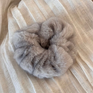 Close-up of soft grey-purple faux fur scrunchie on beige pleated fabric texture