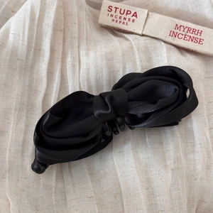 Detail view of a black satin bow banana hair clip on natural linen textured background