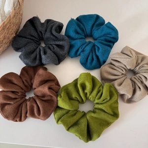 Flat lay of five textured knit scrunchies in gray, blue, caramel, green, and beige tones