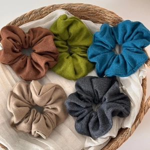 Detail showing five knitted wool hair scrunchies in autumn colors inside a woven basket
