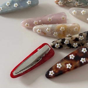 Détail de pinces à cheveux en acétate avec fleurs 3D et structure métallique de bec de canard