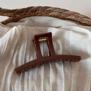 Detail view of large dark brown shark hair claw clip on white textured linen fabric