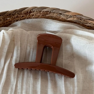 Macro shot of large shiny brown resin hair claw clip on natural woven background