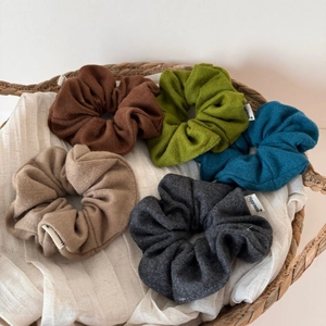 Detail of five wool texture scrunchies in earth tones with Happiness woven labels