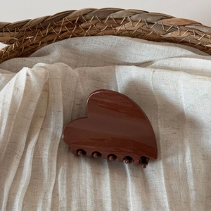 Detail of a brown heart-shaped hair claw clip on soft beige linen fabric texture