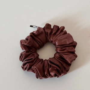 Detail view of dark brown leather scrunchie with silver metal clip and crinkled texture