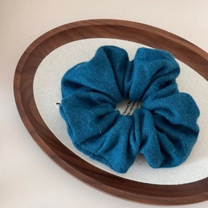 Detailed macro view of peacock blue wool scrunchie texture with a white paper tag