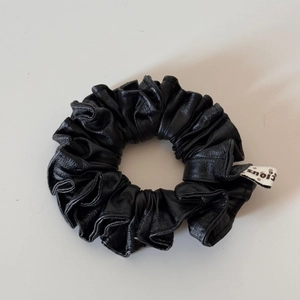 Close-up of black faux leather scrunchie with soft pleats and brand fabric label
