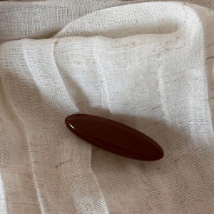 Detail view of large dark reddish-brown glossy hair claw clip on soft beige fabric