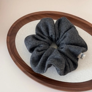 Detailed close-up of dark grey wool fabric scrunchie with happiness label on wooden tray