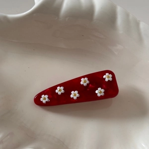 Détail d'une pince à cheveux en acétate rouge avec marguerites blanches sur un plateau
