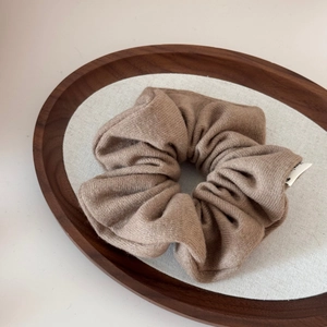 Close-up of a brown knitted wool scrunchie featuring soft texture and a small woven label