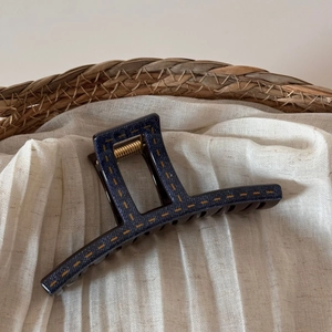 Detail of large dark blue denim-textured hair claw with contrast yellow stitching