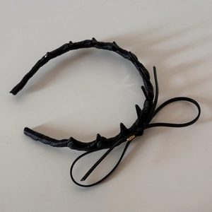 Detail of black leather headband featuring punk spikes, a large bow and gold metal tag