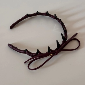 Close-up of a burgundy leather headband with black spiky decor and a slim ribbon bow