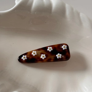 Détail d'une pince à cheveux motif écaille avec des petites fleurs blanches sur plat blanc