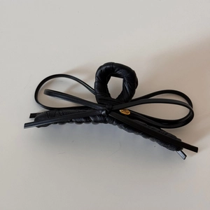 Detail of matte black leather bow hair claw clip featuring a gold Love metal plaque