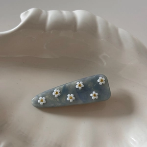 Détail de la barrette en acétate bleu avec fleurs blanches et perles dorées sur plat coquillage