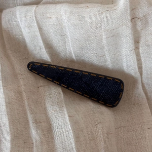 Detail of a navy denim fabric hair clip with yellow stitching on soft linen background