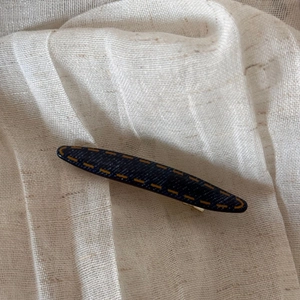 Detail of dark blue denim hair claw with yellow stitching on soft beige linen fabric