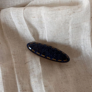 Close-up of dark denim texture hair clip with yellow contrast stitching detail