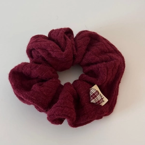 Détail d'un chouchou en maille torsadée rouge foncé avec petite étiquette en tissu à carreaux