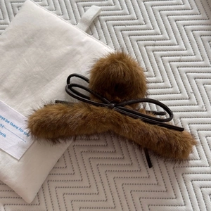 Détail d'une pince à cheveux en peluche marron avec noeud en cuir sur tissu matelassé