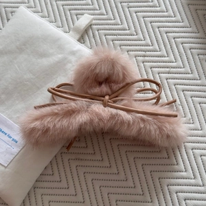 Détail d'une pince à cheveux rose en peluche avec nœud en similicuir sur tissu doux