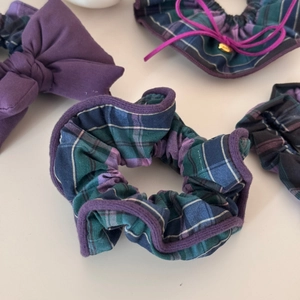 Detail showing blue and purple plaid fabric texture and bow design of the hair scrunchies