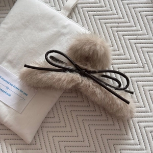 Détail d'une pince à cheveux en peluche avec nœud en cuir marron sur fond en toile