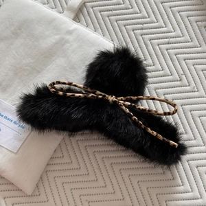 Détail d'une pince à cheveux en peluche noire avec un nœud élégant à motif léopard