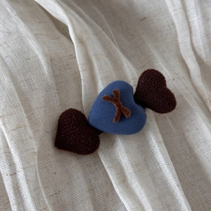 Vue détaillée de la pince à cheveux avec coeurs en tissu bleu et marron sur fond de textile doux