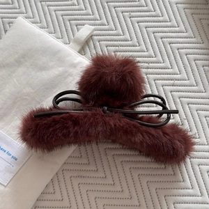 Détail d'une pince à cheveux en peluche bordeaux avec pompons en fourrure et nœud en cuir