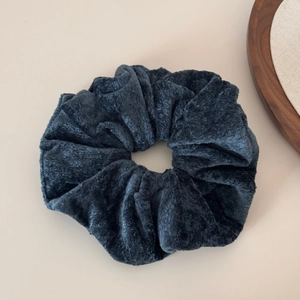 Close-up of dark blue velvet scrunchie showing plush texture and uniform folds on white surface