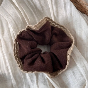 Gros plan d'un chouchou en tricot marron foncé avec bordure en dentelle crème