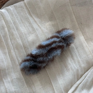 Detail shot of a plush striped hair clip in brown and blue tones on soft linen