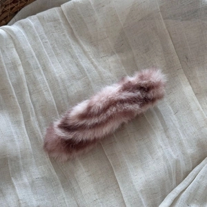 Close-up of a large plush faux fur hair clip in dusty pink on soft linen fabric background