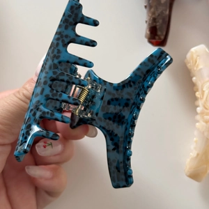 Detail showing hand holding large blue acetate shark hair claw clip with leopard pattern