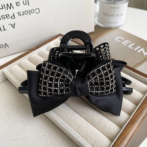Detail of a black satin bow hair claw clip with sparkling rhinestones on a beige velvet tray