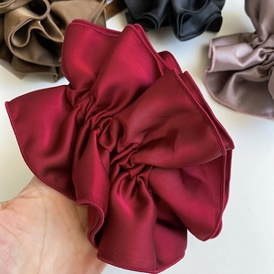 Detailed view of oversized burgundy satin scrunchie showing pleated texture and glossy finish