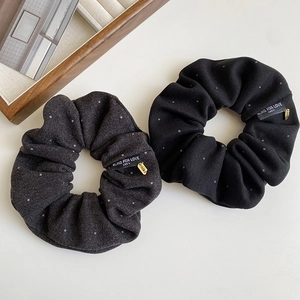 Detail of dark grey and black fabric scrunchies with white lettering labels and gold charms