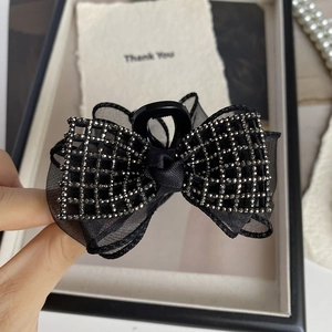 Détail d'une pince à cheveux à nœud en résille noire avec strass et motif à carreaux chic