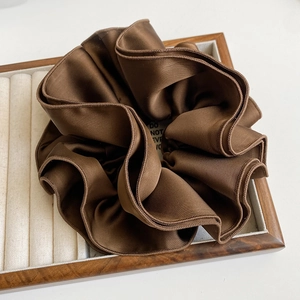 Close-up of chocolate brown satin hair scrunchie with elegant folds on a wooden tray